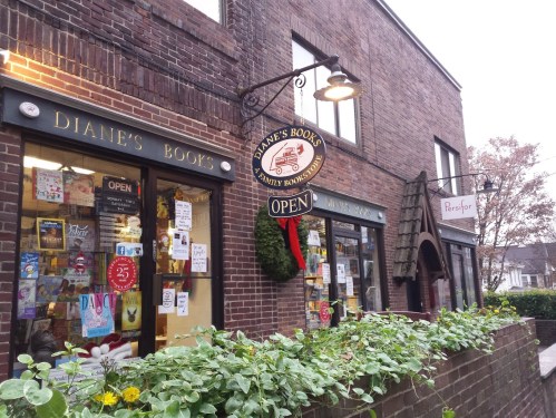A cozy brick storefront with "Diane's Books" and "Renfrew" signs, decorated for the holidays and featuring an open sign.
