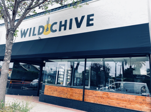 Exterior of a restaurant named "WILDCHIVE," featuring a large sign and wooden seating area.