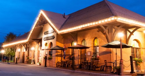 Historic train station illuminated at dusk, featuring outdoor seating and decorative lights.