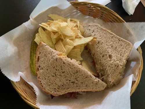 A sandwich with rye bread, sauerkraut, and chips, served in a basket with a pickle on the side.