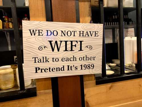 Sign stating "We do not have WiFi. Talk to each other. Pretend it's 1989." displayed in a restaurant.