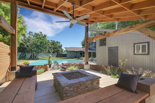 Cozy outdoor space with a fire pit, seating, and a view of a pool surrounded by greenery and a modern home.