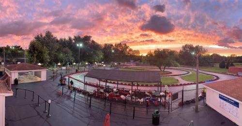 A go-kart track at sunset, with vibrant clouds and trees in the background, and karts lined up near the starting area.