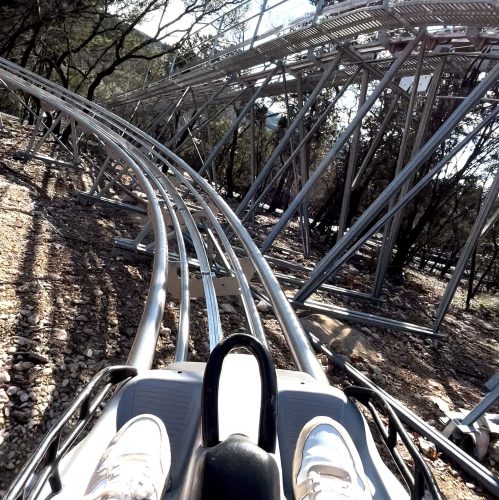 A close-up view from a roller coaster car, showing the track winding through a wooded area.