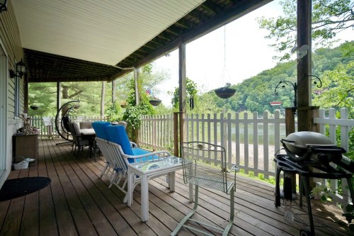 A cozy porch with seating, a grill, and views of a serene river and lush greenery.