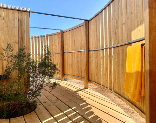 A wooden outdoor space with curved walls, a towel hanging, and a small plant, under a clear blue sky.