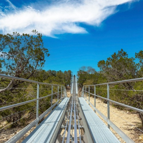 A metal track leads through a wooded area under a bright blue sky with scattered clouds.