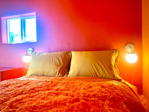 Cozy bedroom with a vibrant orange wall, a fluffy orange bedspread, and soft lighting from two bedside lamps.