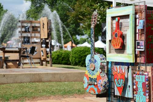 Colorful art displays featuring guitars and heart designs at an outdoor festival with fountains in the background.