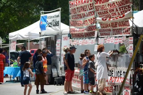 A busy food festival scene with vendors, families, and children enjoying various food stalls under colorful tents.