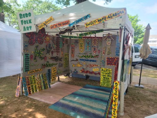 Colorful folk art display featuring painted wooden items and vibrant signs in a tent at an outdoor market.
