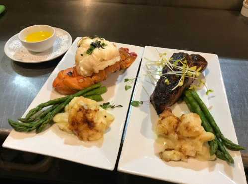 Two elegant plates of seafood and steak, featuring lobster, asparagus, and creamy sides, with a small bowl of sauce.