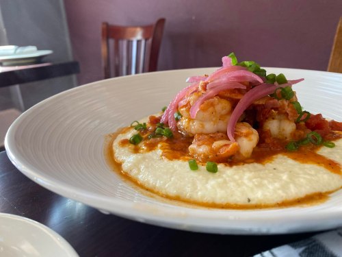 A plate of shrimp atop creamy grits, garnished with pickled onions and green onions, served in a restaurant setting.