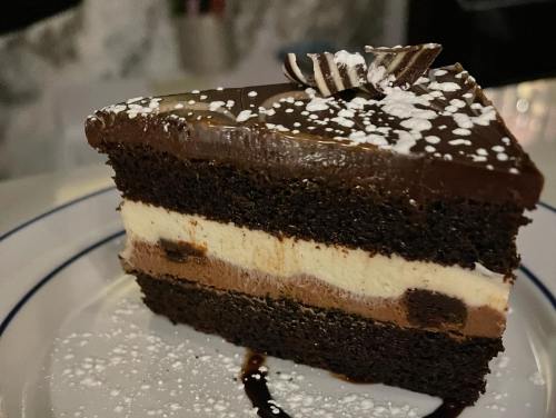 A slice of layered chocolate cake with cream filling, topped with chocolate shavings and powdered sugar.