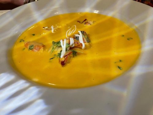 A creamy yellow soup garnished with herbs and drizzled with sauce, served in a white bowl.