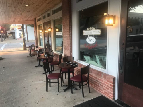 Outdoor seating area of a bistro with empty tables and chairs along a brick sidewalk.