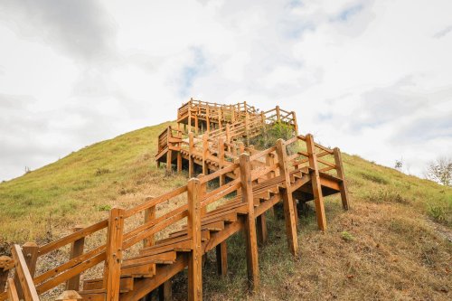 Wooden stairs winding up a grassy hill under a cloudy sky.