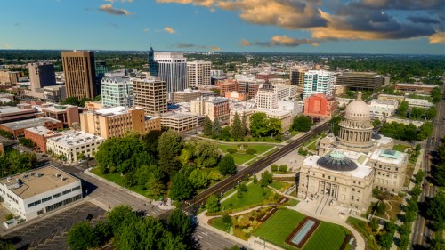 Aerial view of a city skyline with modern buildings, green parks, and a prominent dome structure under a blue sky.