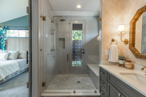 Modern bathroom featuring a glass shower, gray tiles, and a stylish vanity with natural light from a nearby window.