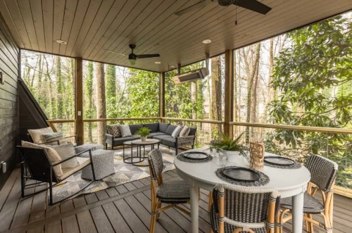 A cozy screened porch with a dining table, seating area, and greenery visible through the screens.