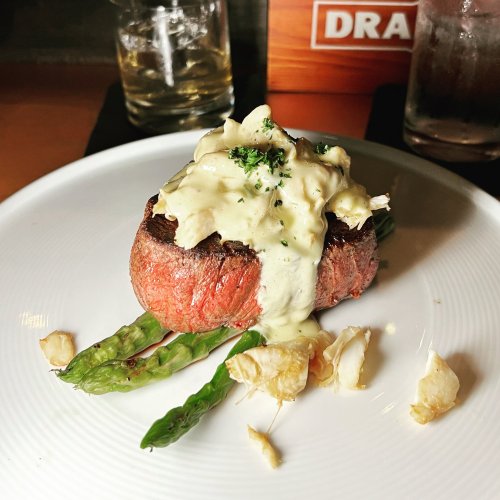 A perfectly cooked filet mignon topped with creamy sauce, served on asparagus with garnishes on a white plate.