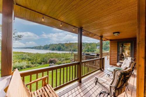 A cozy porch with rocking chairs overlooks a serene lake and lush greenery under a partly cloudy sky.
