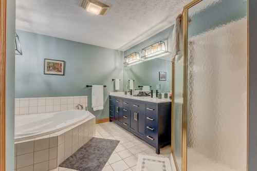 Spacious bathroom featuring a large tub, dual sinks, and a glass shower, with light blue walls and modern fixtures.