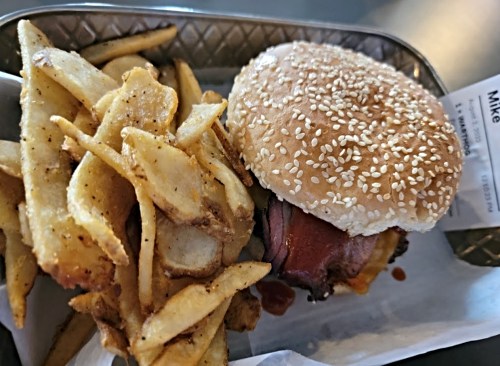 A sesame seed bun burger with bacon and cheese, served with a side of crispy fries on a tray.
