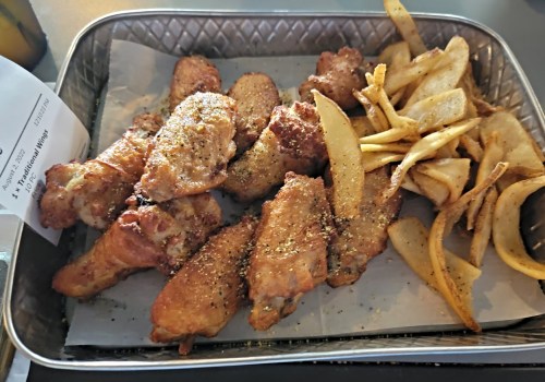 A metal tray filled with crispy chicken wings and golden fries on a sheet of paper.
