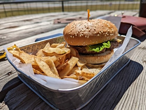 A sesame seed burger with lettuce and a side of crispy fries in a metal tray on a wooden table.