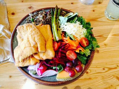A colorful plate featuring fried fish, mixed greens, asparagus, tomatoes, carrots, beets, grapes, and wild rice.