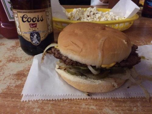 A hamburger with onions, pickles, and cheese next to a bottle of Coors beer, with popcorn in the background.