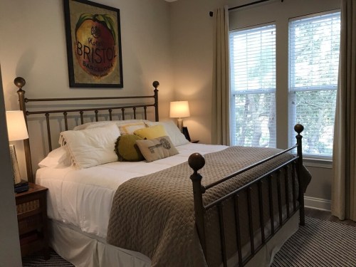 Cozy bedroom with a brass bed, yellow and gray bedding, two lamps, and large windows letting in natural light.