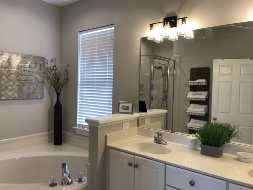 A modern bathroom featuring a large mirror, sink, shower, and decorative plants in a stylish, neutral color scheme.
