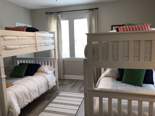 A cozy bedroom with two sets of bunk beds, colorful pillows, and large windows letting in natural light.