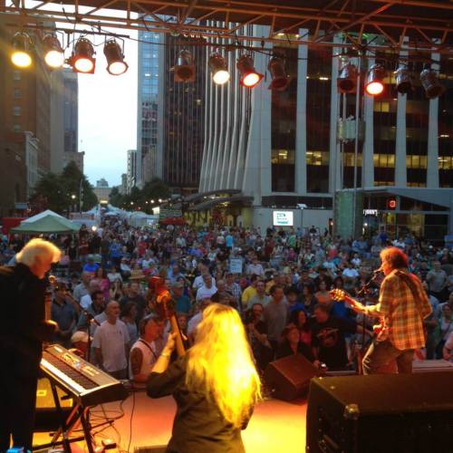 A lively outdoor concert scene with a large crowd enjoying a performance on a city street at dusk.