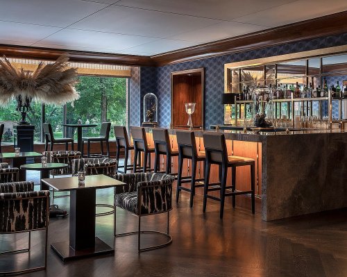 Elegant bar area with stylish seating, dark wood accents, and large windows overlooking greenery.