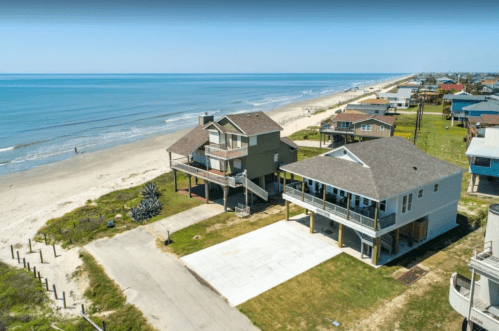 Aerial view of beach houses near a sandy shore, with the ocean and a beach path in the background.