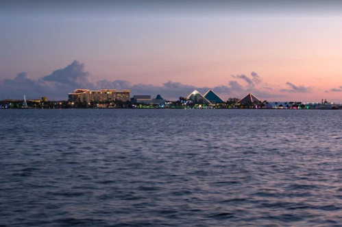 A serene waterfront view at dusk, featuring a skyline with illuminated buildings and pyramidal structures.