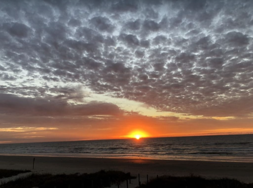 A vibrant sunset over the ocean, with colorful clouds reflecting the light, and a sandy beach in the foreground.