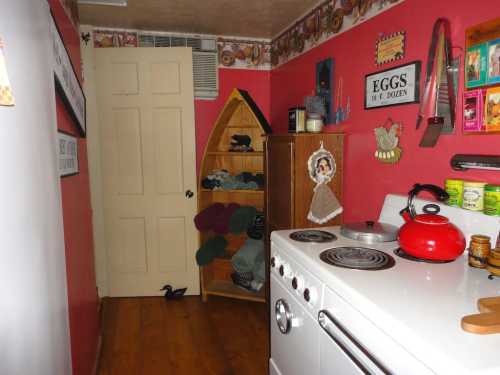 A cozy kitchen with red walls, a vintage stove, a wooden shelf, and a door leading to another room.