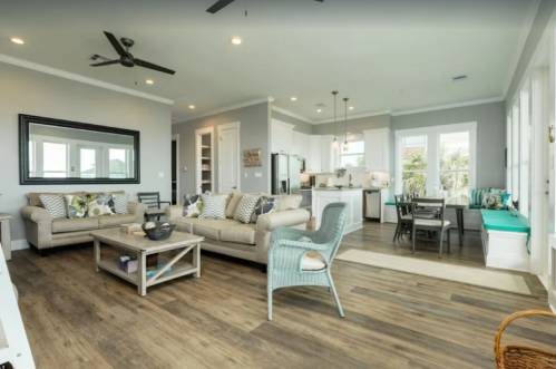 Bright, modern living room with a cozy sofa, dining area, and large windows showcasing a beach view.