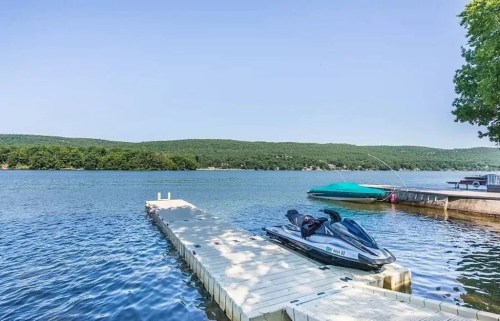 A jet ski parked on a dock by a calm lake, surrounded by green hills under a clear blue sky.