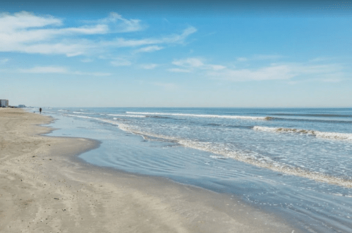 A serene beach scene with gentle waves, soft sand, and a clear blue sky.