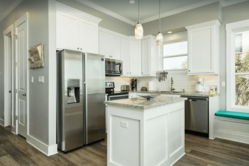 Modern kitchen with white cabinets, stainless steel appliances, and a granite island, featuring natural light and a cozy nook.