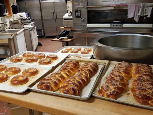 Freshly baked bread loaves and rolls on trays in a commercial kitchen, with ovens and equipment in the background.