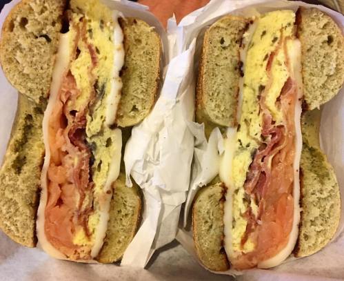 Two bagels filled with layers of smoked salmon, cream cheese, and scrambled eggs, served in a paper wrapper.