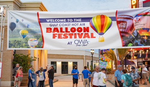 Banner welcoming visitors to the Gulf Coast Hot Air Balloon Festival at OWA, featuring colorful balloons and attendees.
