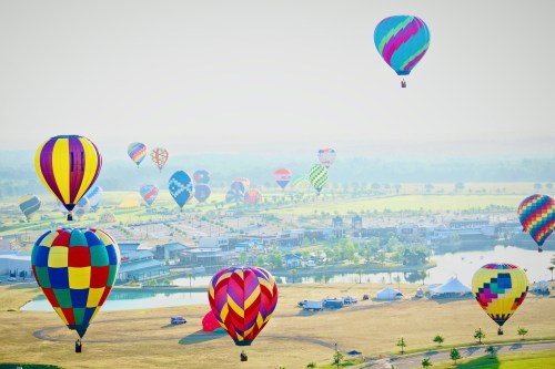 A vibrant scene of colorful hot air balloons floating over a landscape with fields and a lake below.