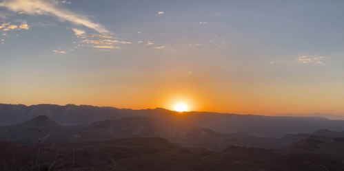 A stunning sunset over mountains, with vibrant orange and yellow hues illuminating the sky.